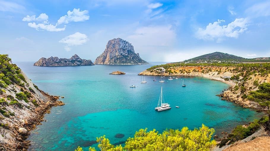 The Balearic Sea with boats sailing above, and Ibiza’s coast with sandy shores, greenery, and Es Vedra