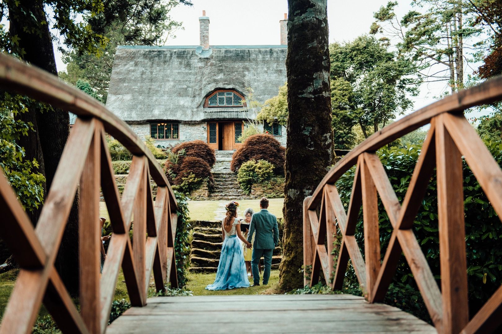 Couple having an elopement ceremony in Ireland in front of a rustic thatched-roof cottage with a bridge in the foreground