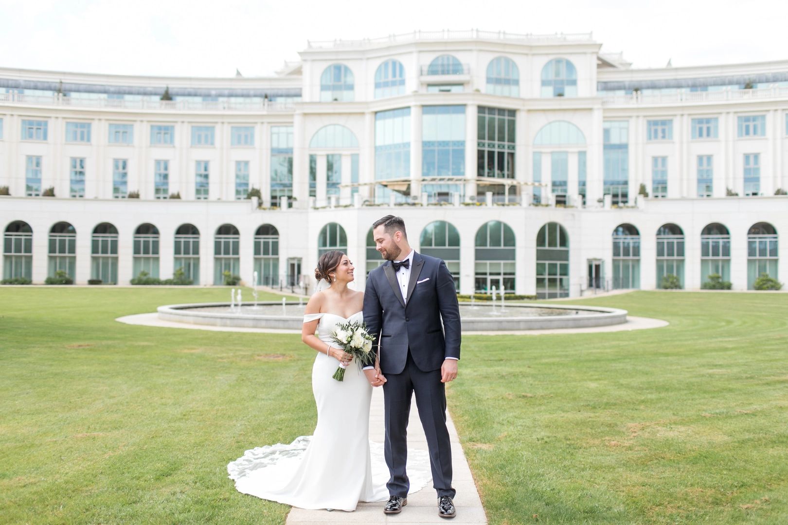 Bride and groom looking at eac other in front of a white palace hotel with a wide lush space in front during their small wedding in Ireland