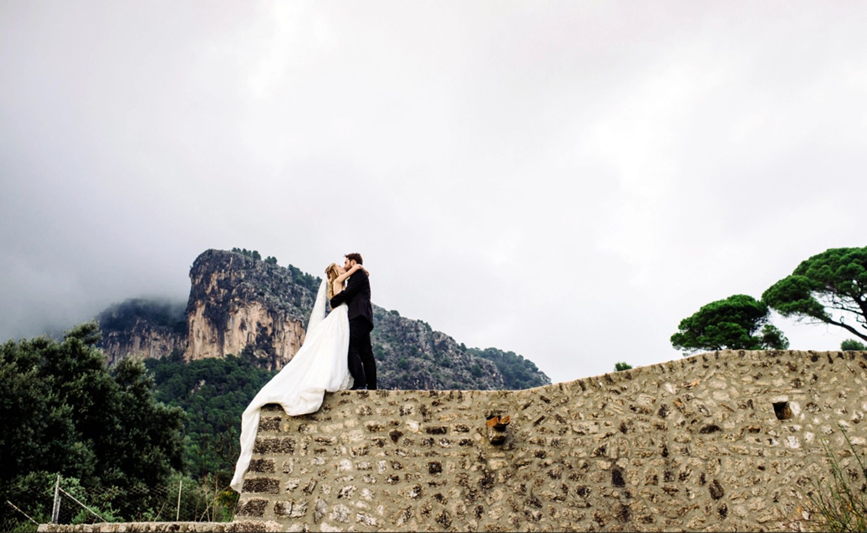Andalusian cliffs in the background while the newlyweds kiss atop a retaining wall 