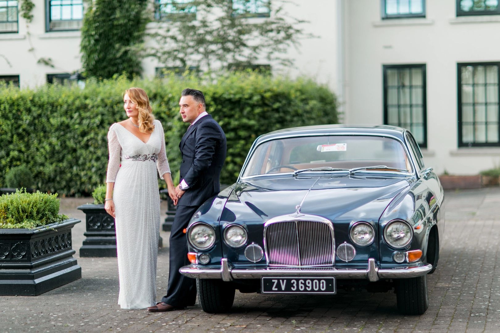 Bride with her groom sitting on a black luxury car in front of a villa