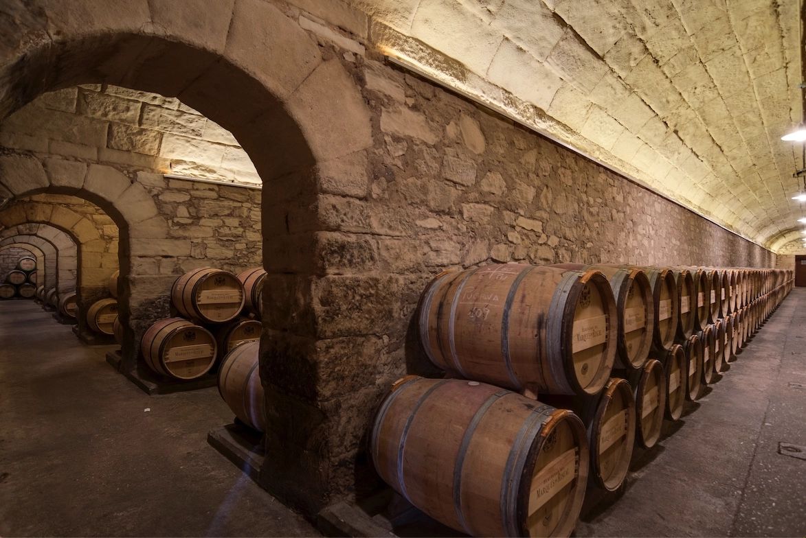 A bodega with medieval walls where many wine barrels are piled up