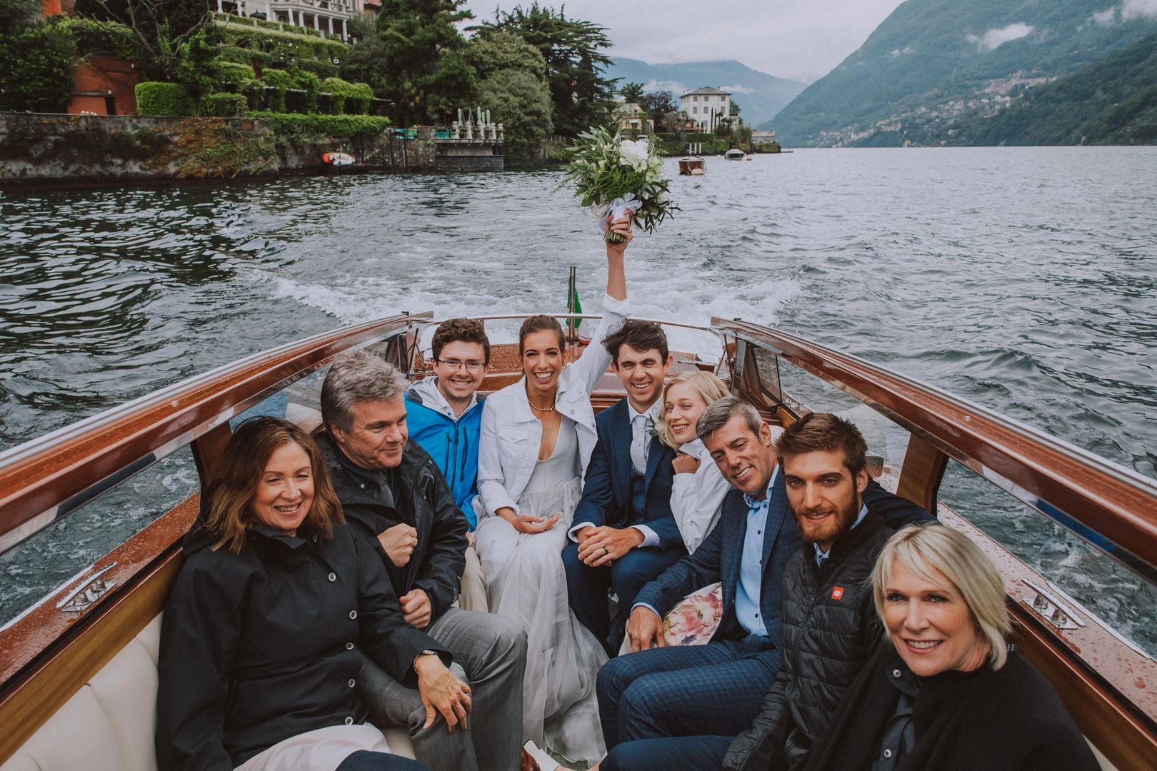 Bride and groom ride a boat with their guests as they happily sail along Lake Como