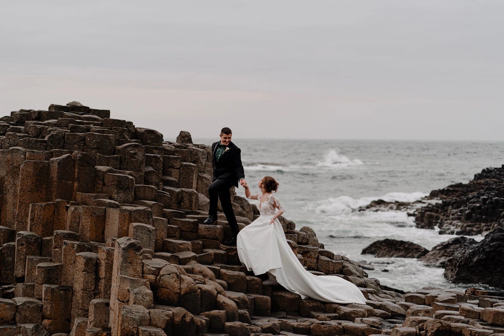 Bride and groom climbing up the basalt columns in the Giant’s Causeway during their elopement in Ireland