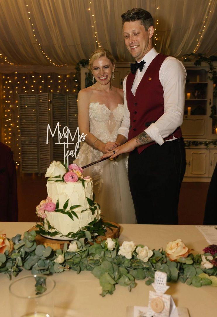 Bride and groom slicing their white two-tiered wedding cake with a sword during their wedding reception in Spain