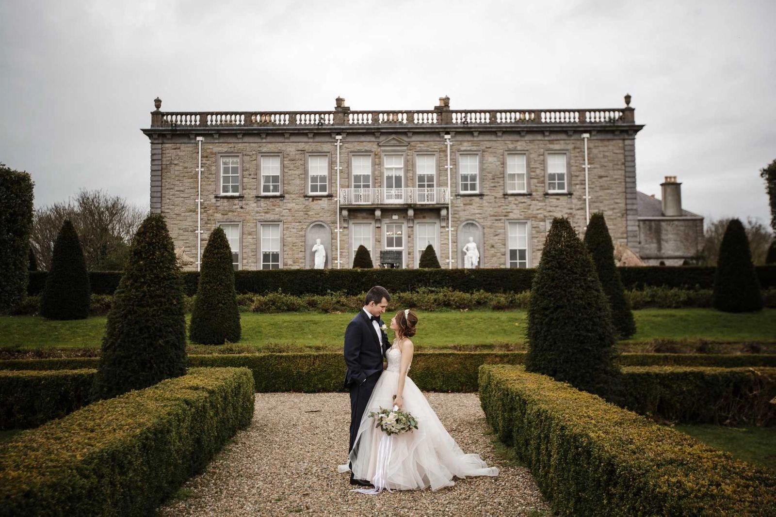 Bride and groom in front of a formal garden of a luxury palace hotel during their destination wedding in Ireland