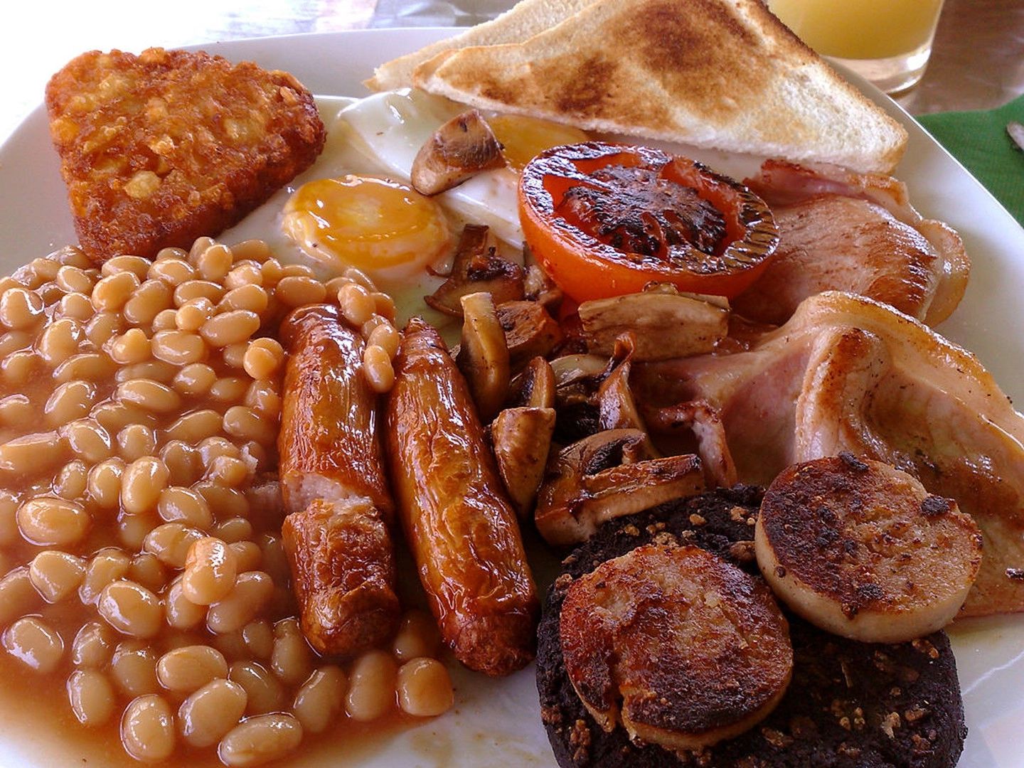 A large plate of Irish breakfast consisting of eggs, bacon, sausages, and beans in tomato sauce