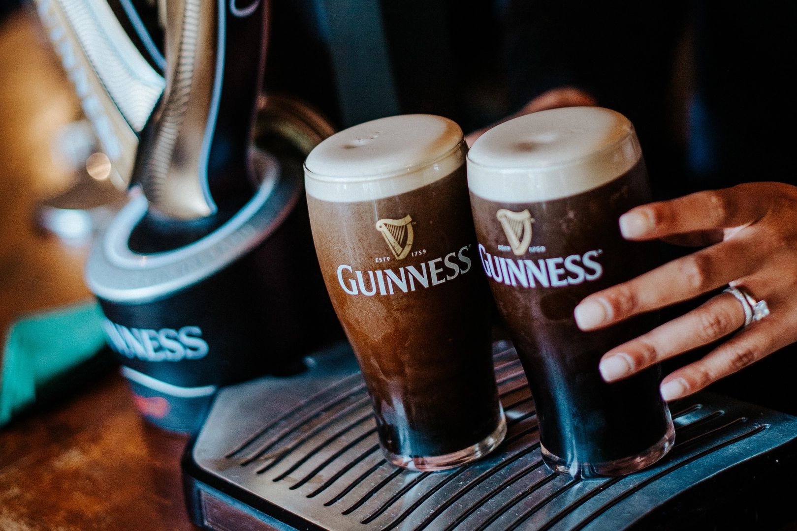 Two glasses of Guinness beer, one is held by a woman’s hand with rings