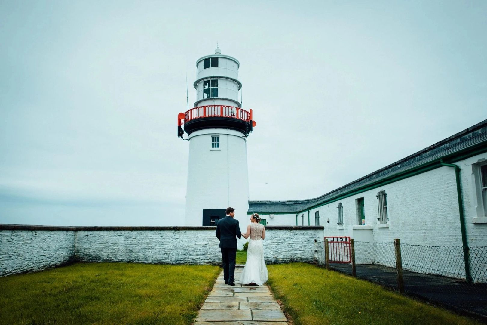 Newlyweds walking towards a lighthouse in Ireland during their Irish destination wedding