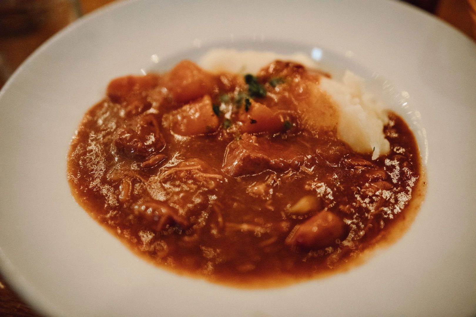 Lamb stew in red sauce and a scoop of potatoes in a white plate