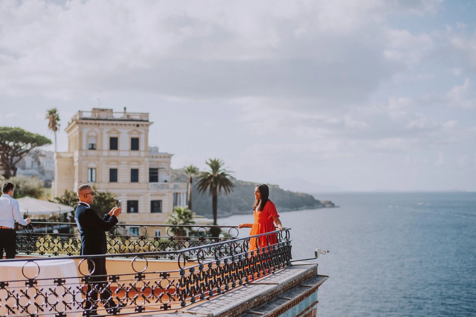 Lady in an orange dress having her photo taken by a male while they are on top of a terrace overlooking the Bay of Naples on the edge