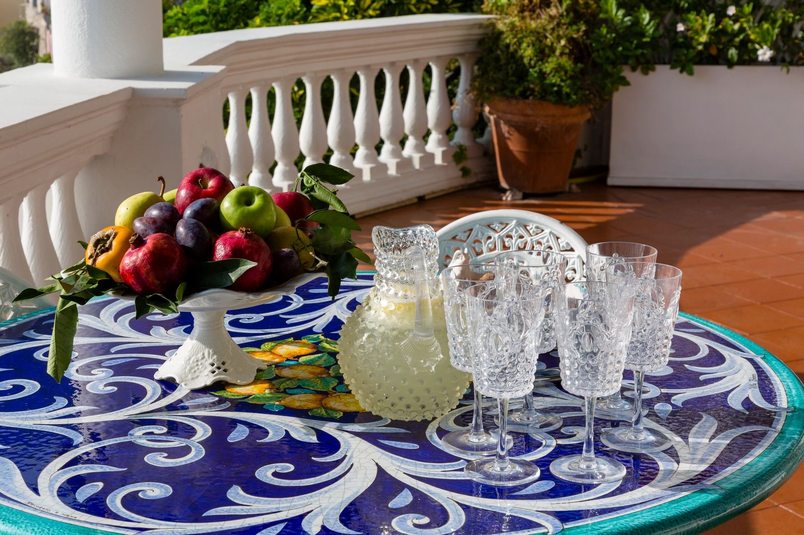 Table with blue linen with a tray of fruits, a pitcher of lime sorbetto with empty glasses