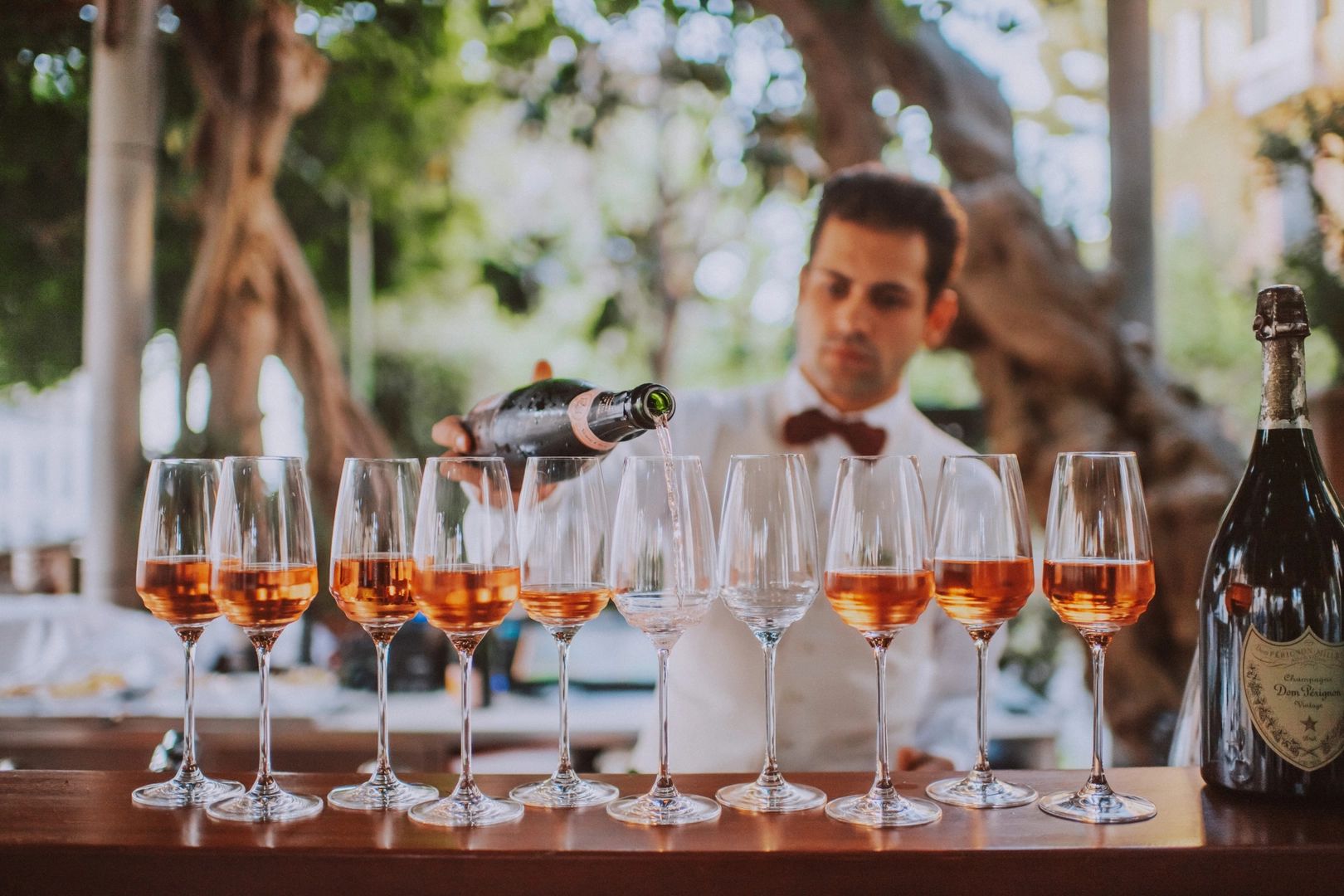 A bartender pouring liquor in several wine glasses