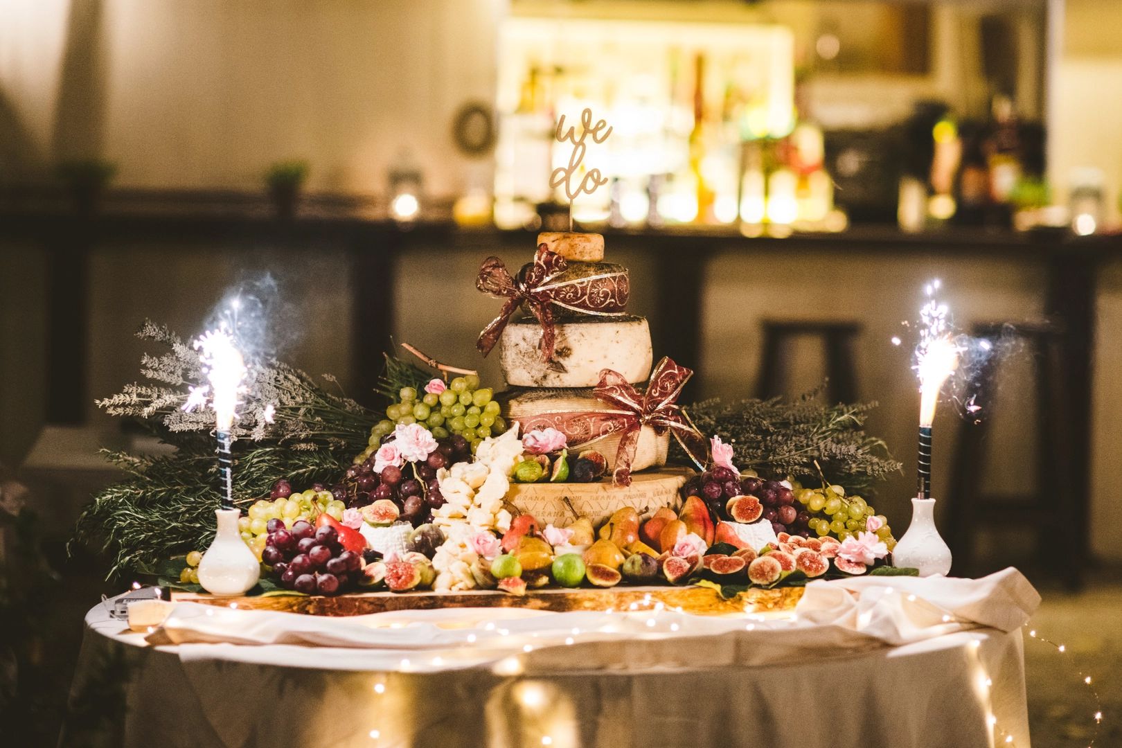 Three-tiered wedding cake made of cheese, surrounded with fruits with two sparklers on both sides