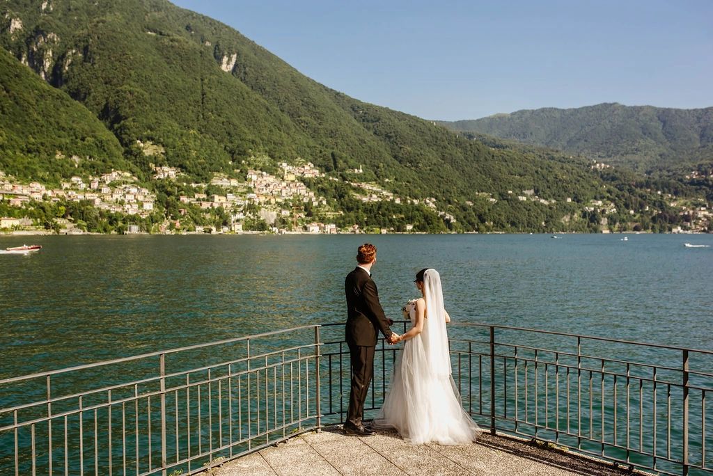 Bride and groom at the edge of a terrace looking at Lake Como, the lakeside villages, and rolling hills