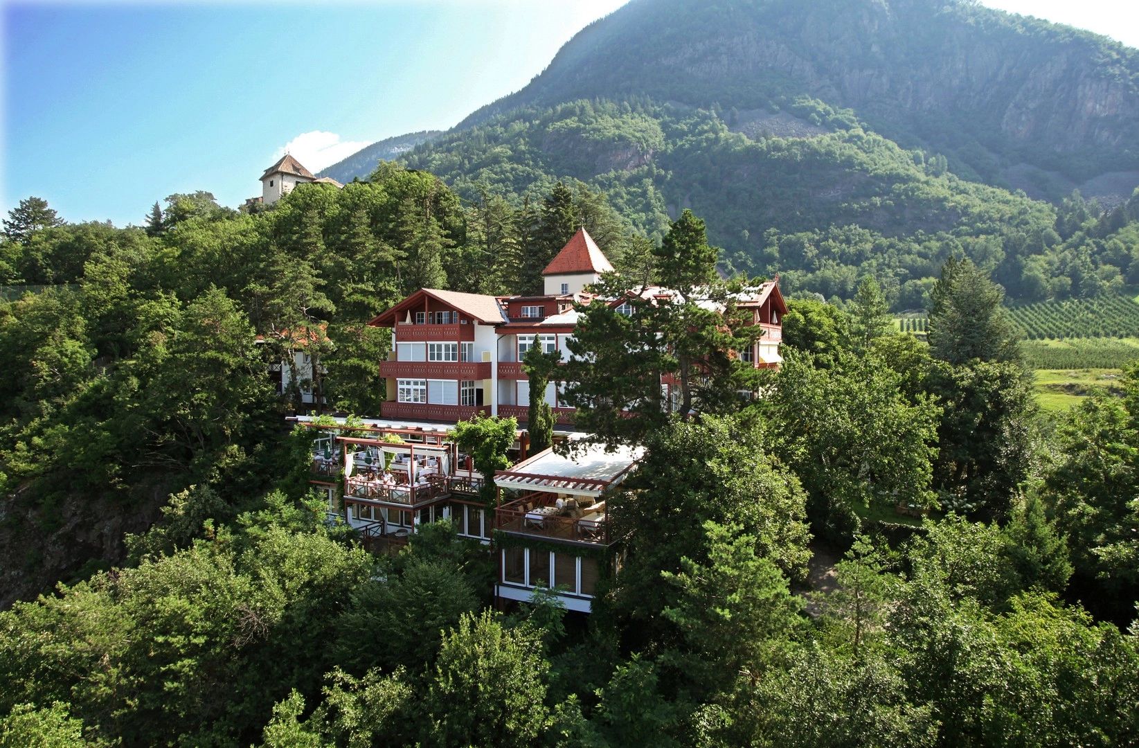 A hilltop hotel surrounded by forests, tall trees, vineyards, and mountains in Italy’s Dolomites region