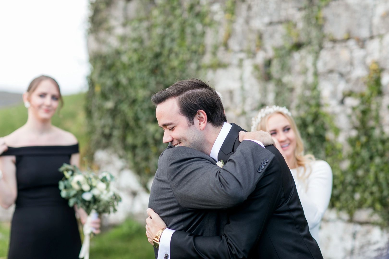 Bride's father hugging the groom during a wedding ceremony with two women in the background