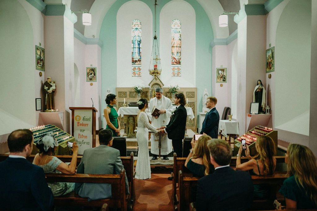 Bride and groom having a wedding ceremony in front of a priest and their guests inside a Catholic church in Ireland