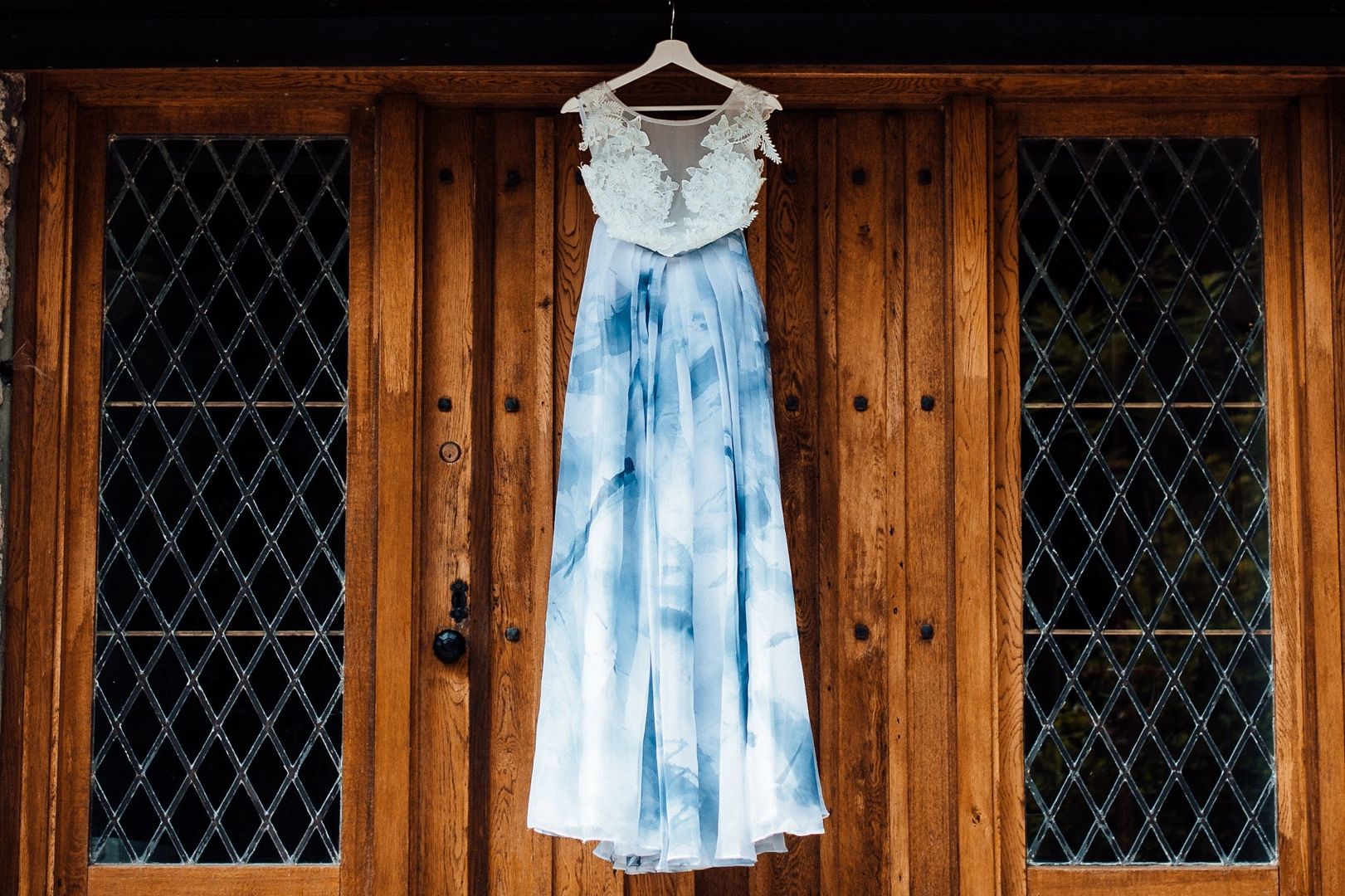 A casual wedding dress with a white lace top and a blue-dyed long skirt hung next to a wooden door of a cottage