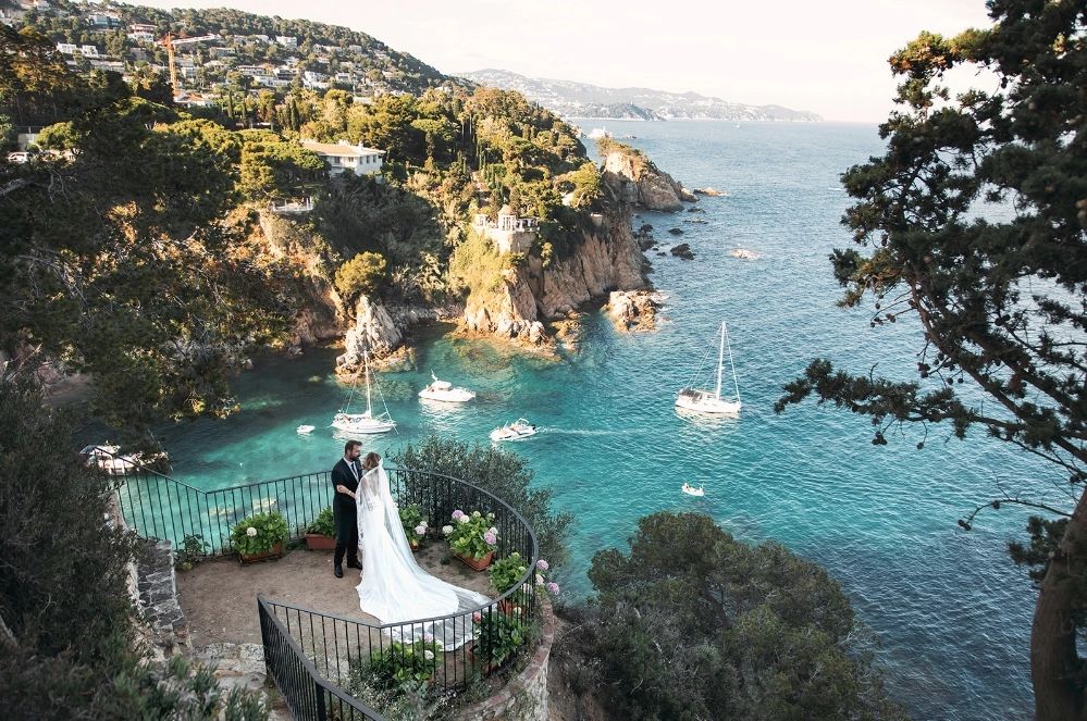 Newlyweds at a terrace of a villa with views of the Mediterranean Sea, rocky cliffs, and lush hillsides