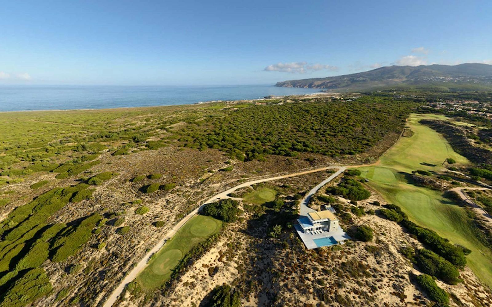 Drone shot of a coastal landscape in Portugal showing forests, green open fields, and a villa with a pool