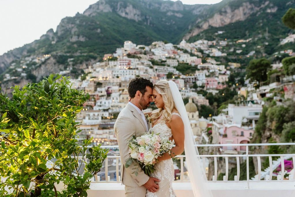 Newlyweds on top of a terrace of a hotel overlooking the pastel buildings of Amalfi Coast