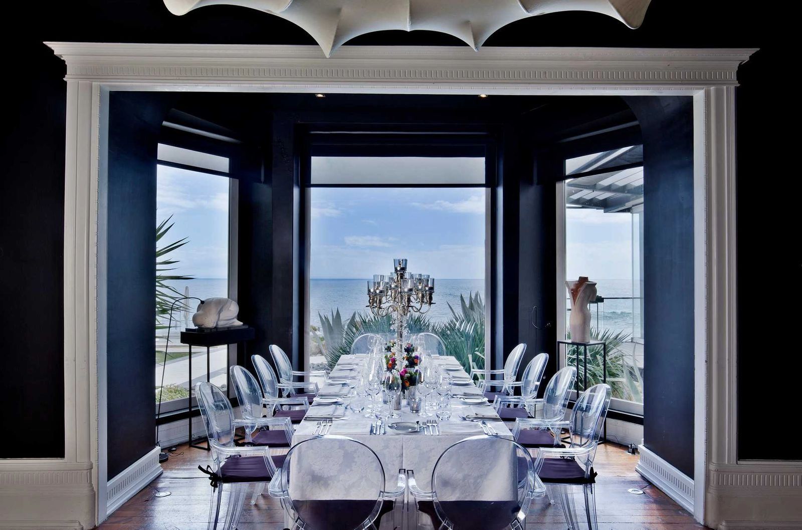 A hotel’s function room with a long table and glass chairs inside and glass walls overlooking the beach outside in Algarve, Portugal