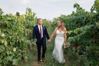 Bride and groom holding hands whilst walking aong vineyards at their intimate wedding in Italy