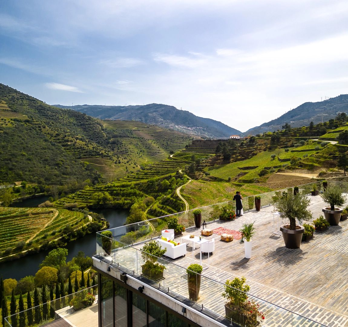 The terrance vineyards of the Douro Valley and a terrace of a hotel with a couple on top, looking at the scenic view