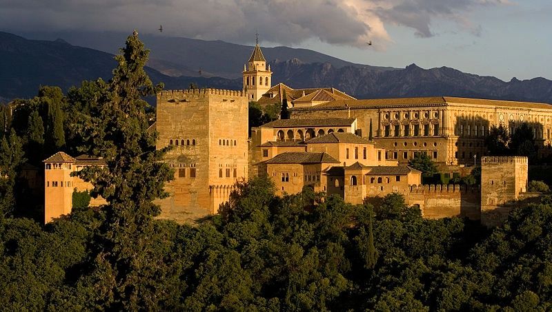 A 14th-century complex made of Roman fortifications in Alhambra, Spain that’s surrounded by trees, with mountains in the background