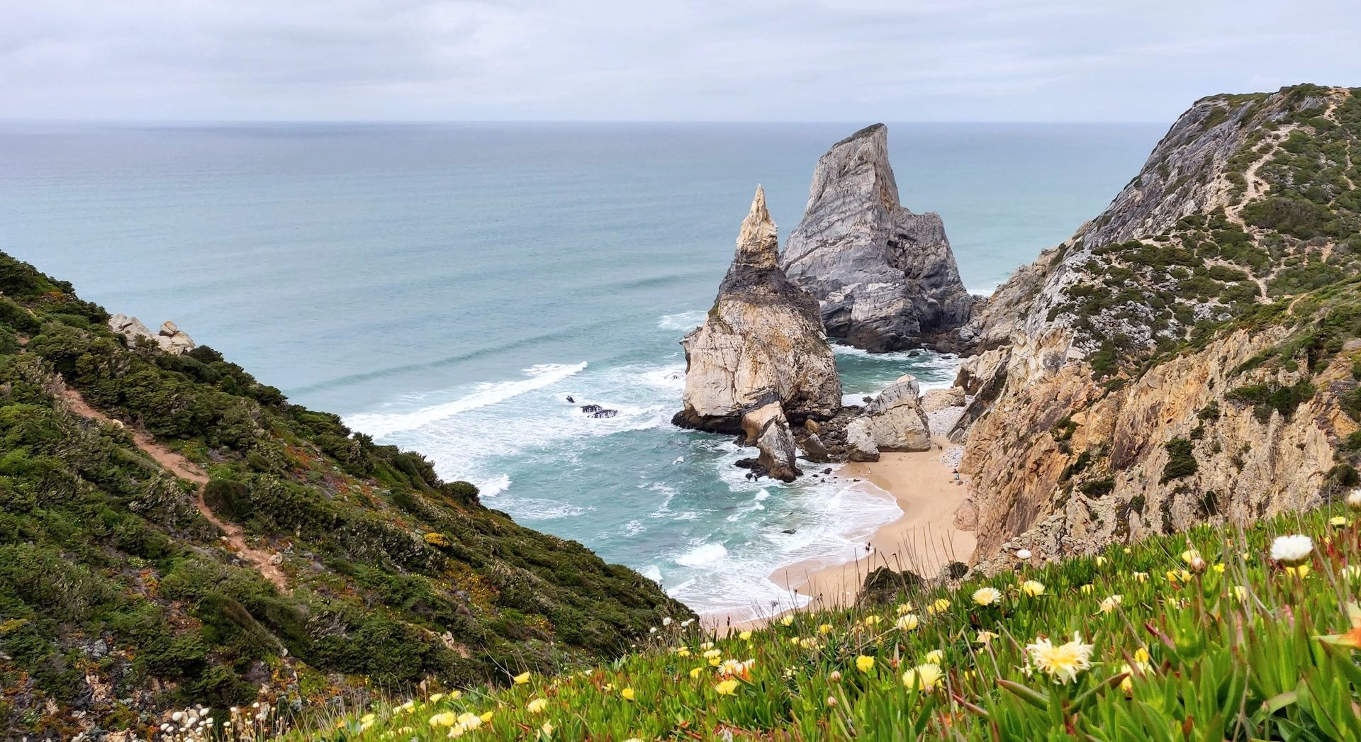 A white-sand beach with big rocks and cliffs covered with greenery in Sintra, Portugal