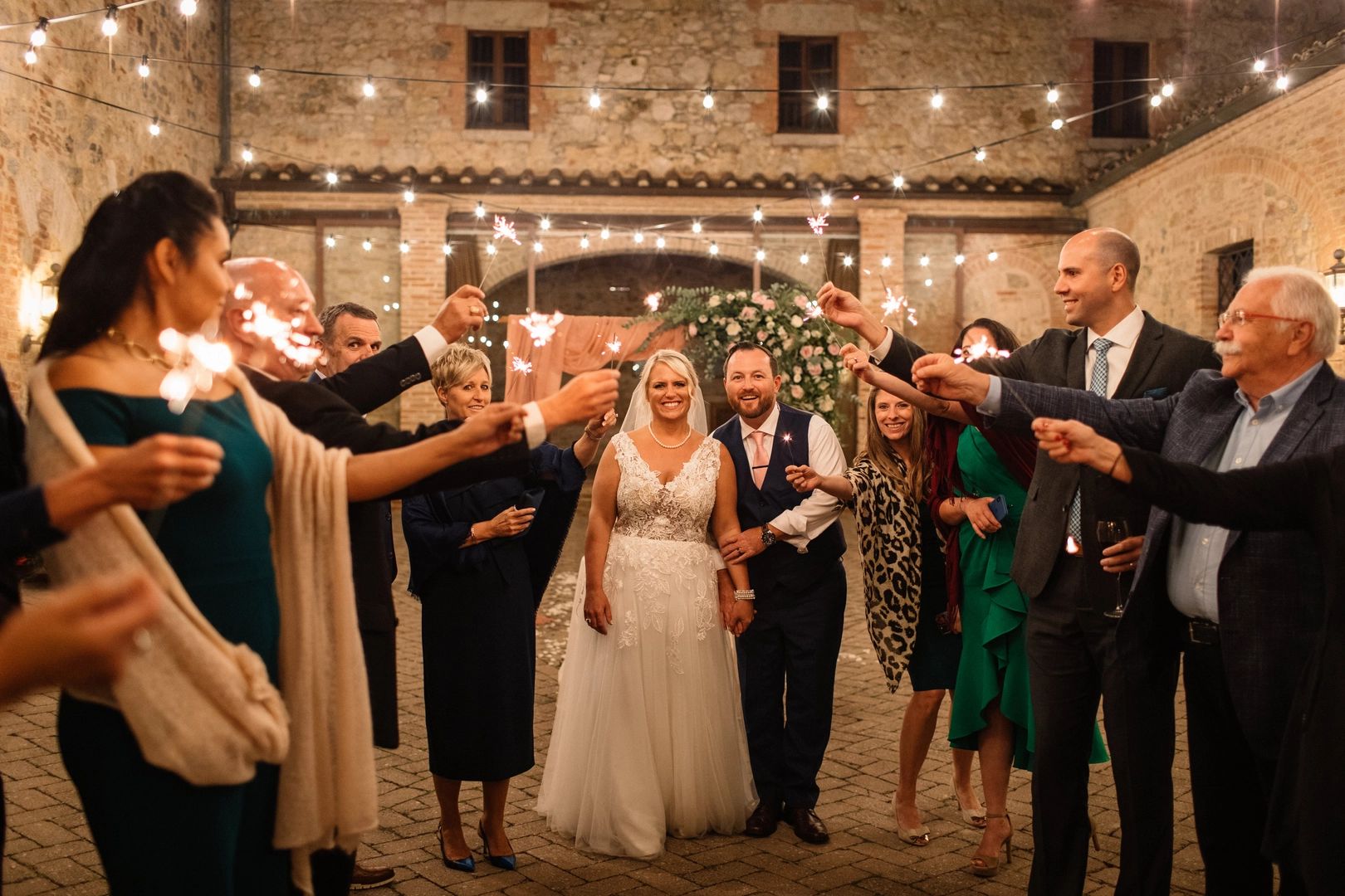 Bride and groom surrounded by their wedding guests who are holding sparklers while celebrating