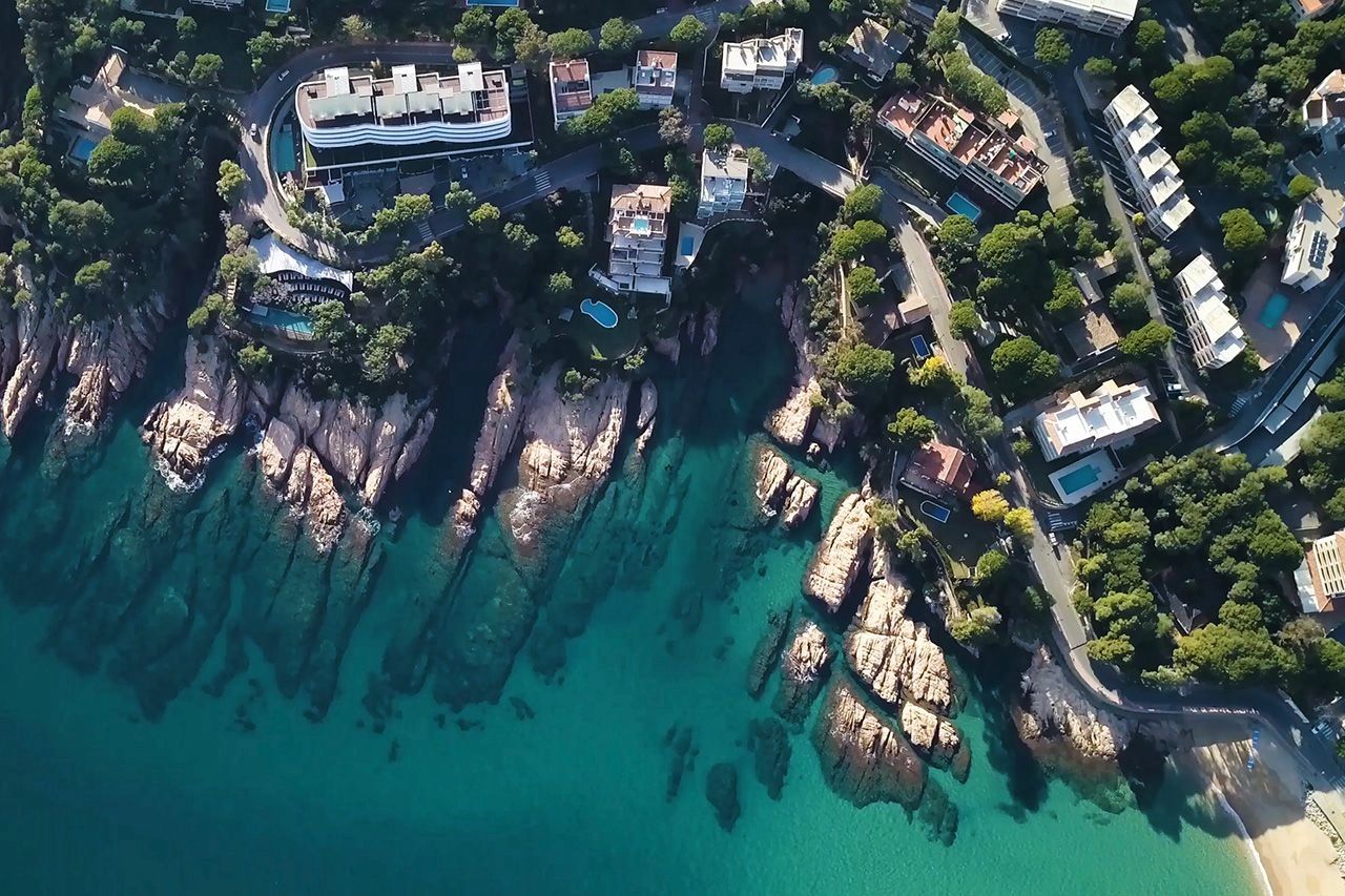 An aerial shot of hotels perched on seaside rocks and turquiose waters on the edge