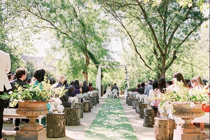 Wide open space with tall trees where a wedding ceremony is happening with guests seated in white chairs