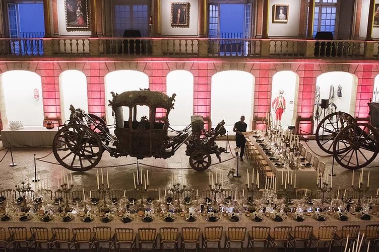 A museum in Portugal with ancient horse carriages serves as an event room, with chairs and tables arranged for a wedding reception