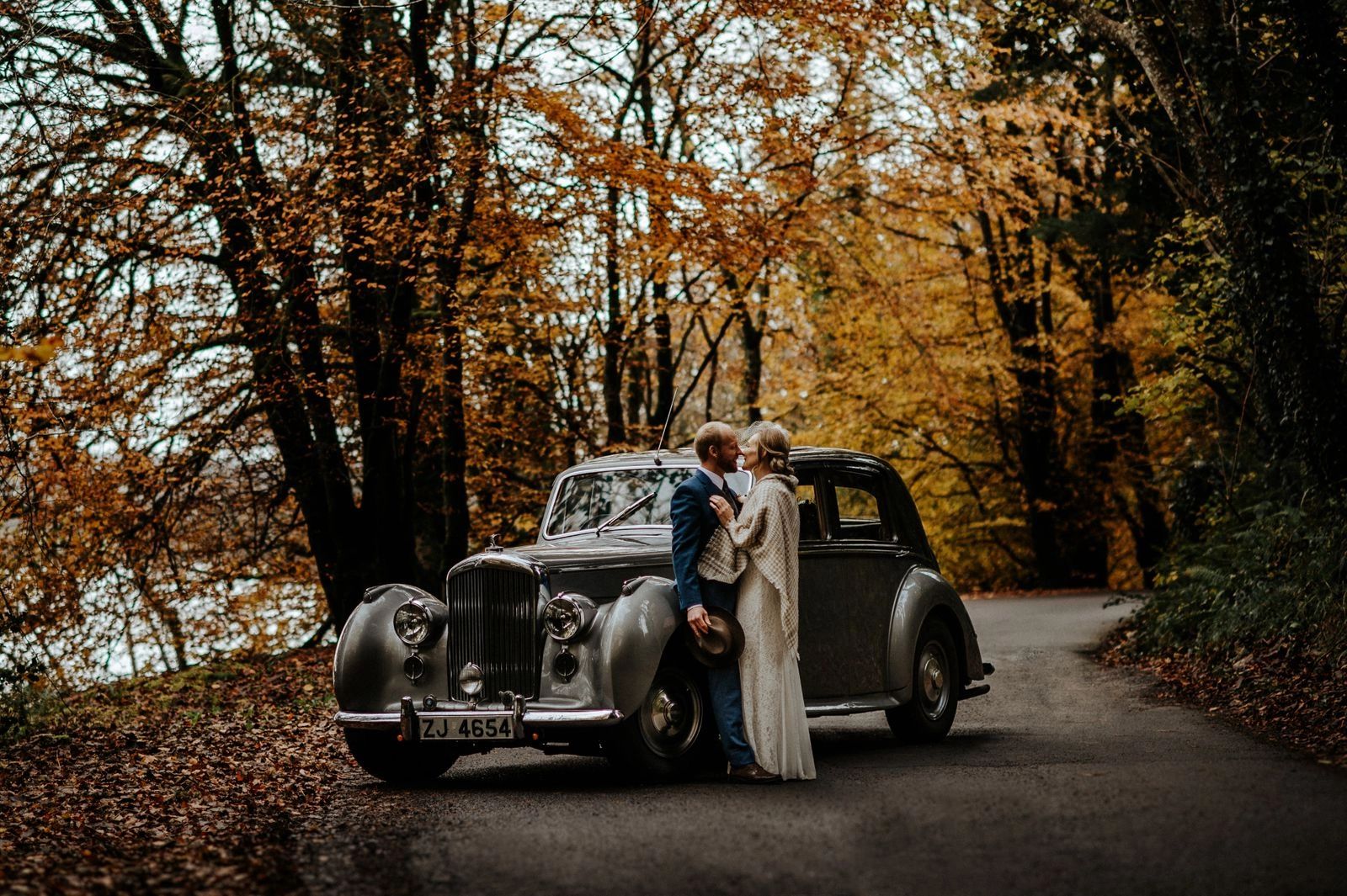 Newlyweds having a photoshoot for their elopement in Ireland with a vintage car and vibrant autumn colors in the background