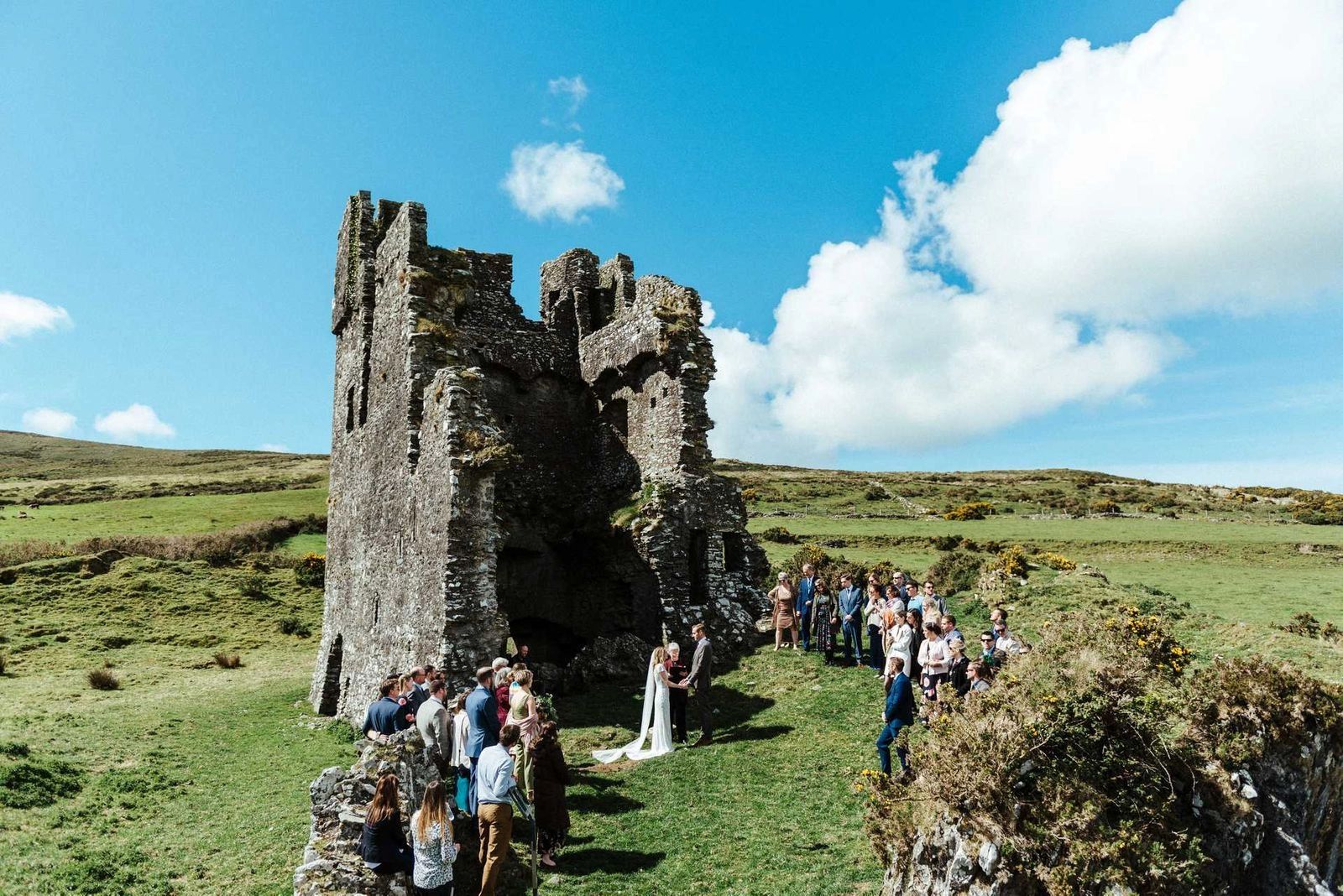 An intimate ceremony in front of a castle ruin under clear skies in Ireland