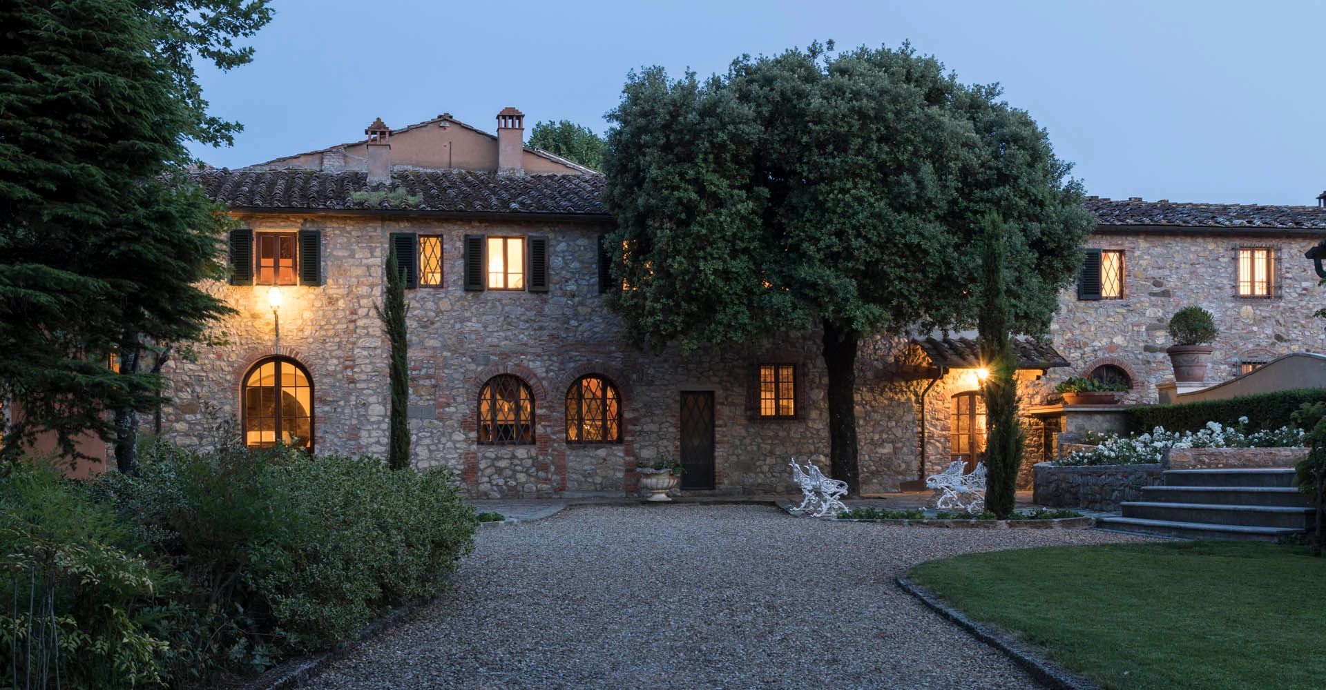 Farmhouse and resort in Tuscany surrounded by trees, with lights inside the rooms.