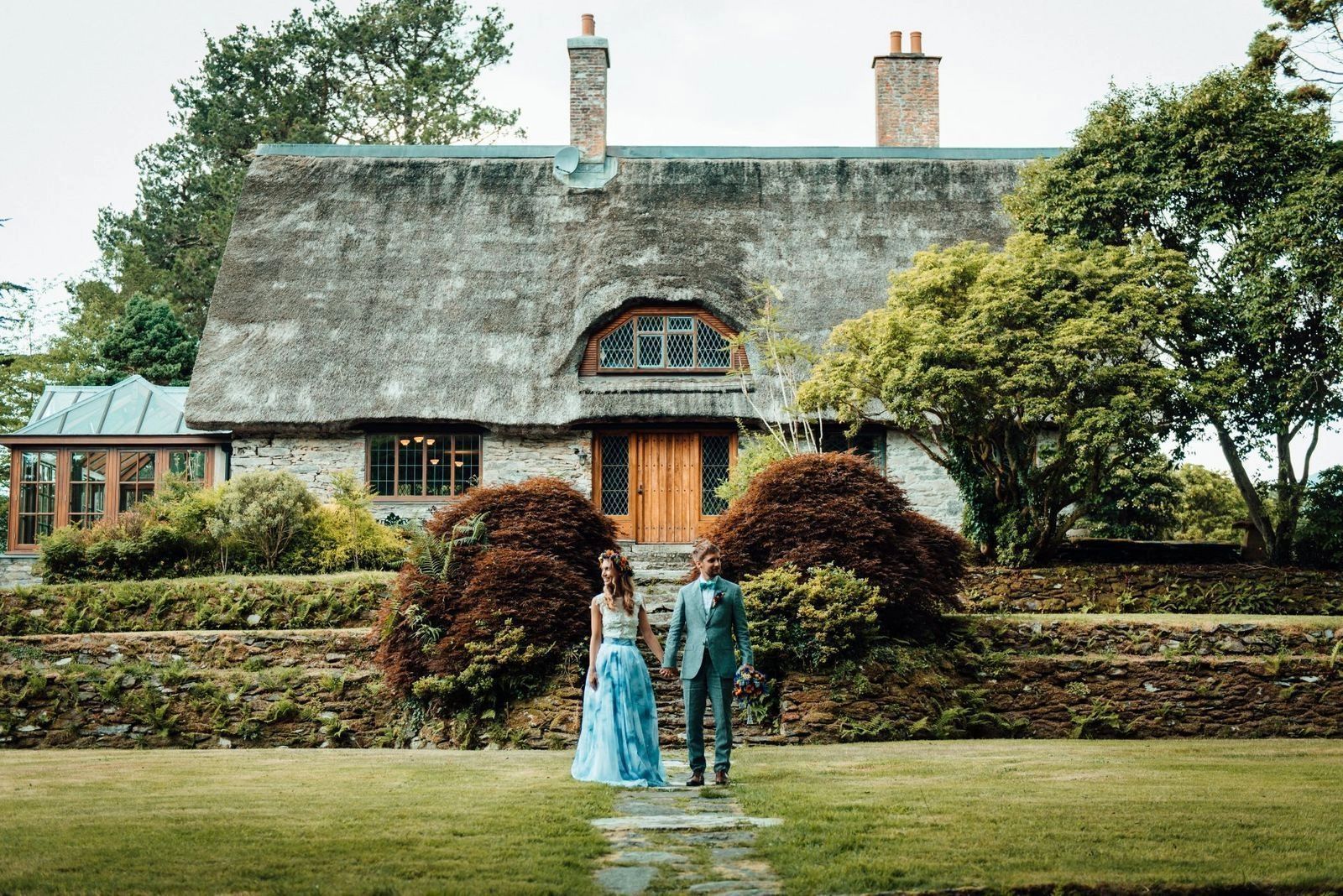 Newlywed couple holding hands in front of a rustic cottage in Ireland