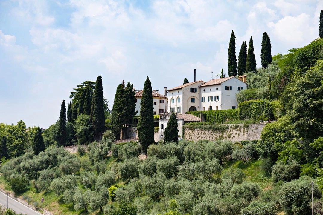 White villa on top of a hill surrounded by lush greenery in Italy