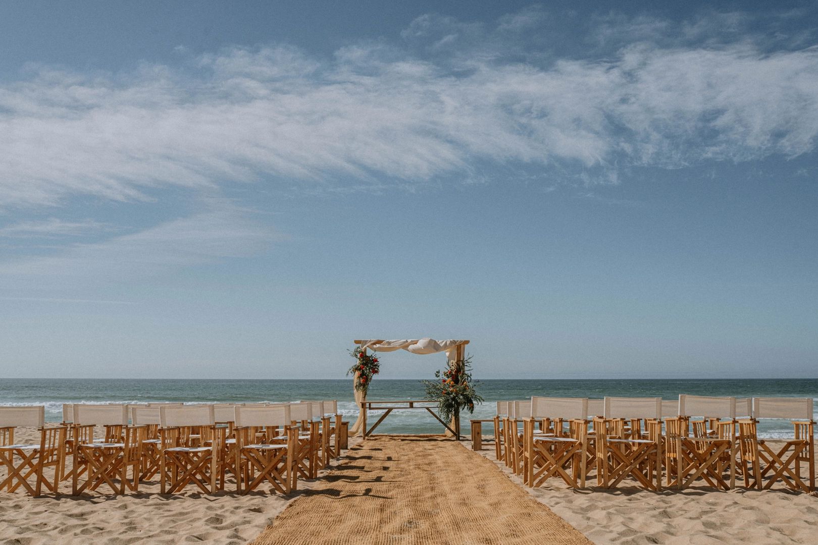 Wooden chairs and a wooden wedding arch by the beach in Silveira arranged for a ceremony of a destination wedding in Portugal