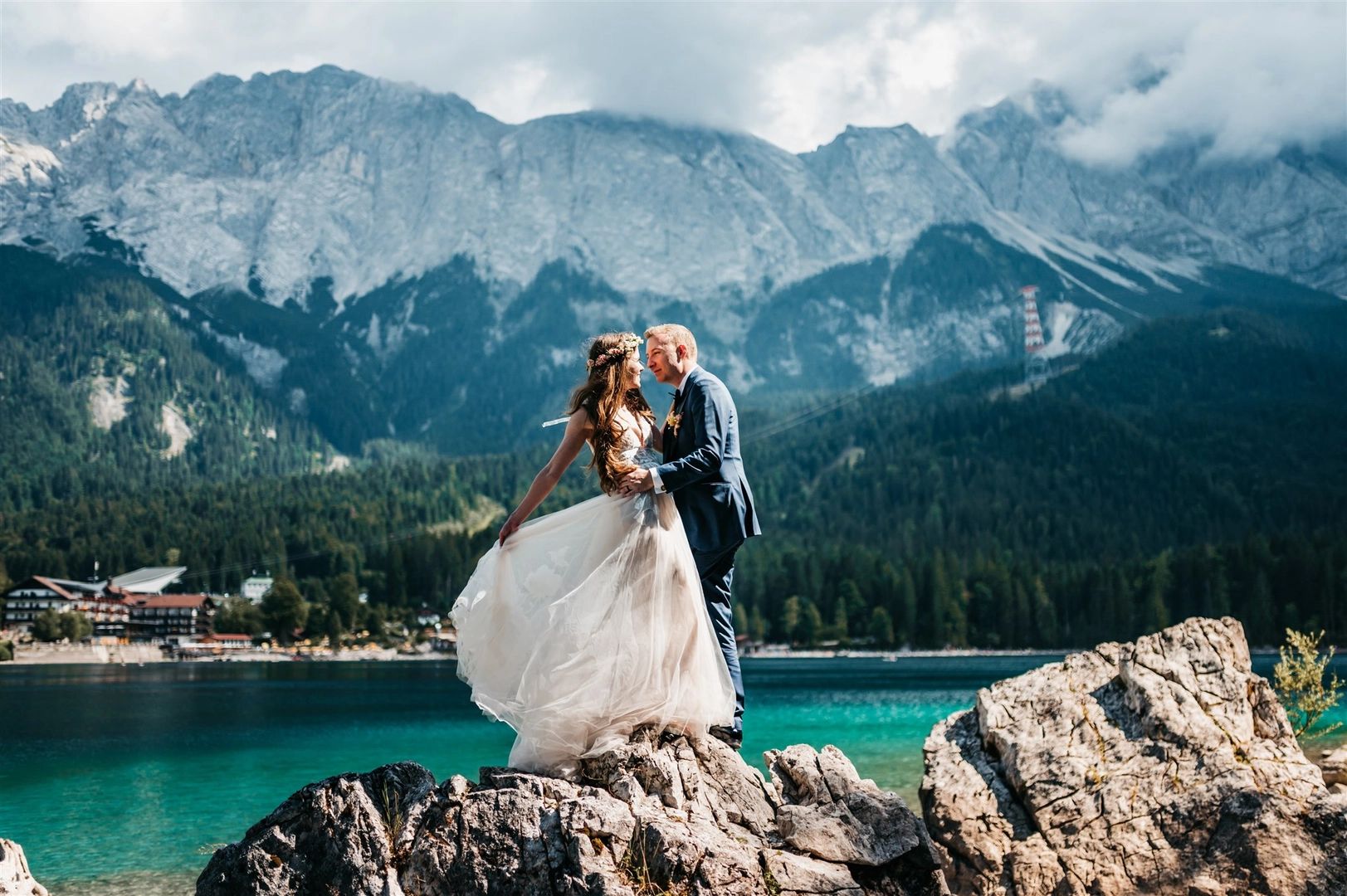 Newlyweds standing atop a rock along with alps and lake in the background