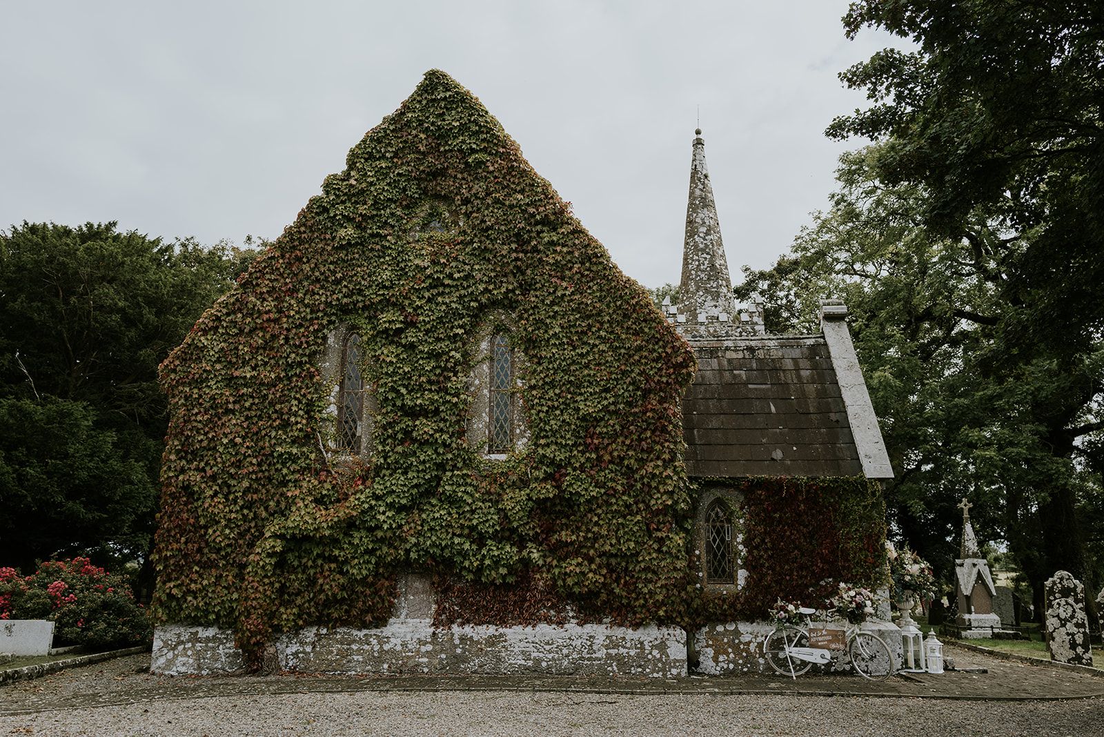 St. John's Church, Knockainey, a creeper-covered wedding venue in County Limerick, with its spire, porch and a white bicycle dressed in flowers by the door.