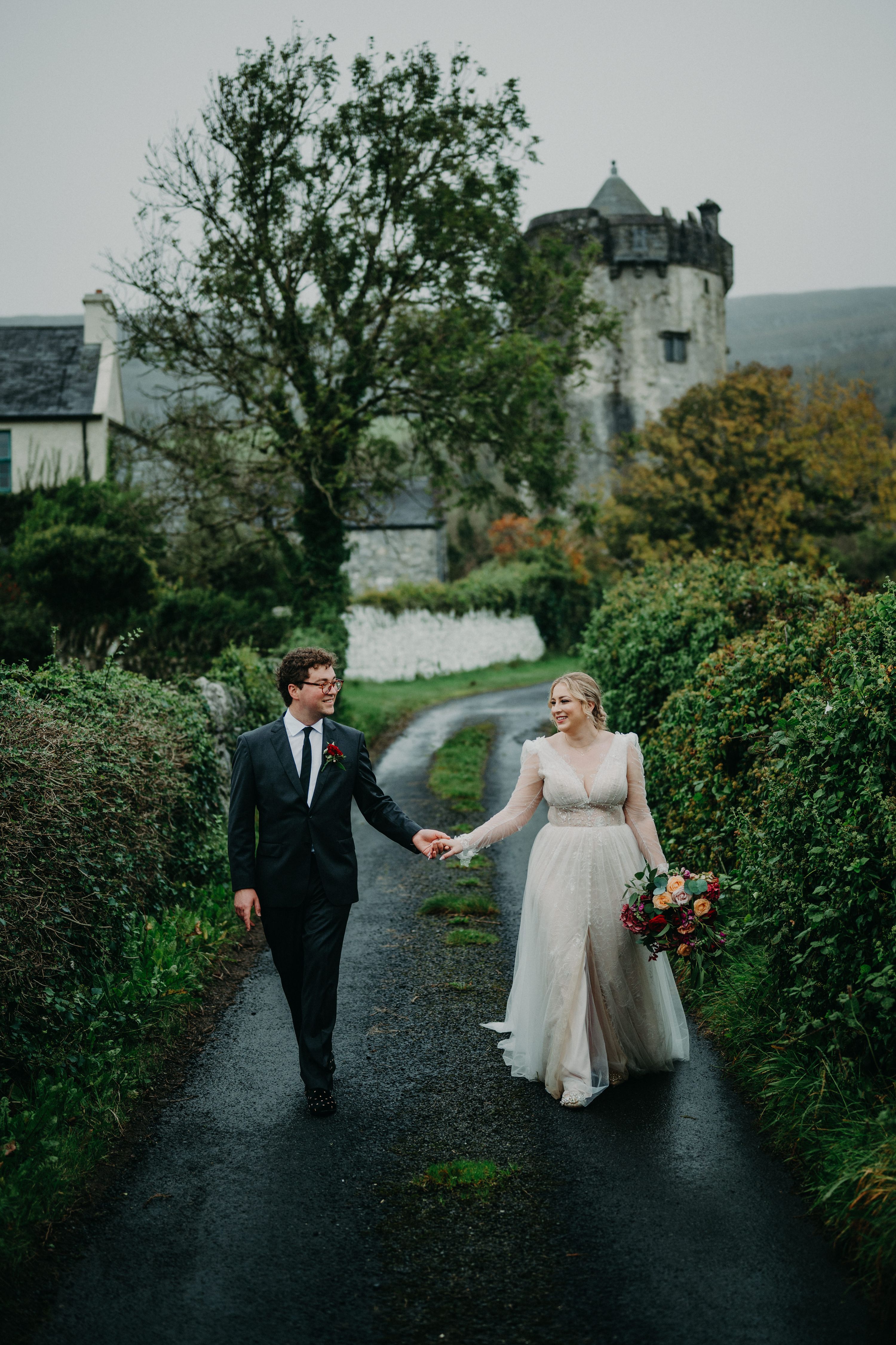 Couple walking hand in hand along a scenic Irish lane near a castle after their small wedding in Ireland