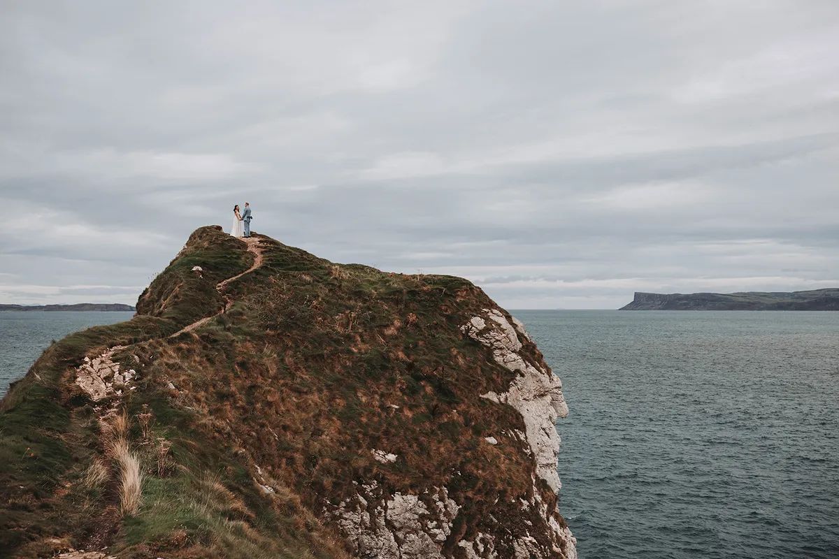 Newlyweds atop the cliffs during their autumn destination wedding in Northern Ireland, with Atlantic Ocean as the backdrop