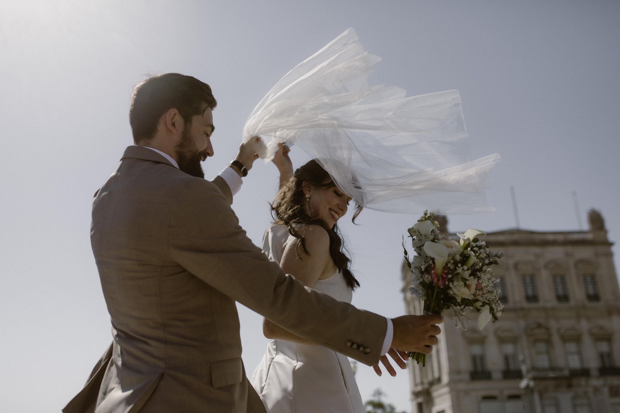 A groom helping his bride to adjust the wedding veil on a windy day