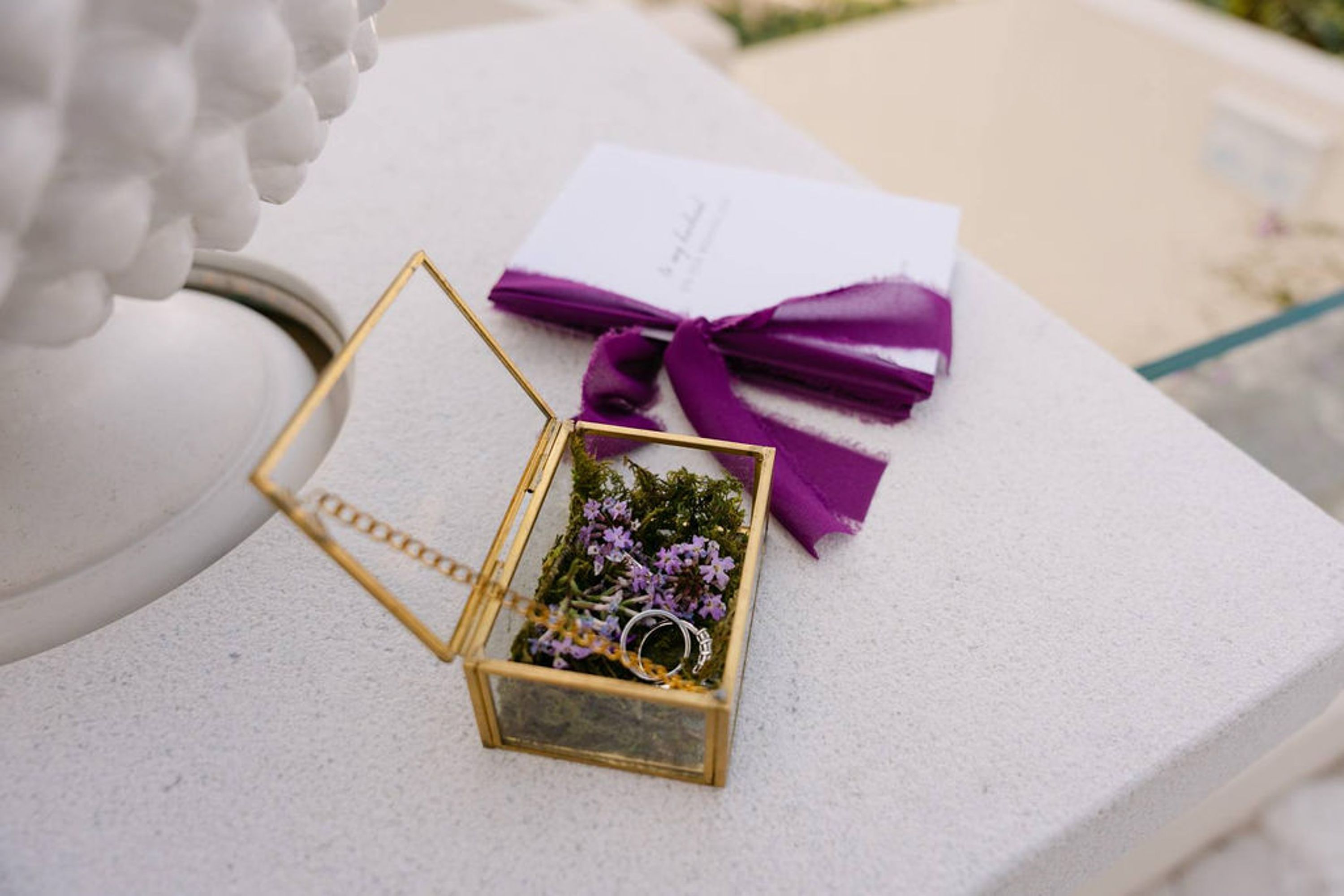 Wedding rings displayed in a glass ring box with invitation details for an intimate wedding in Italy