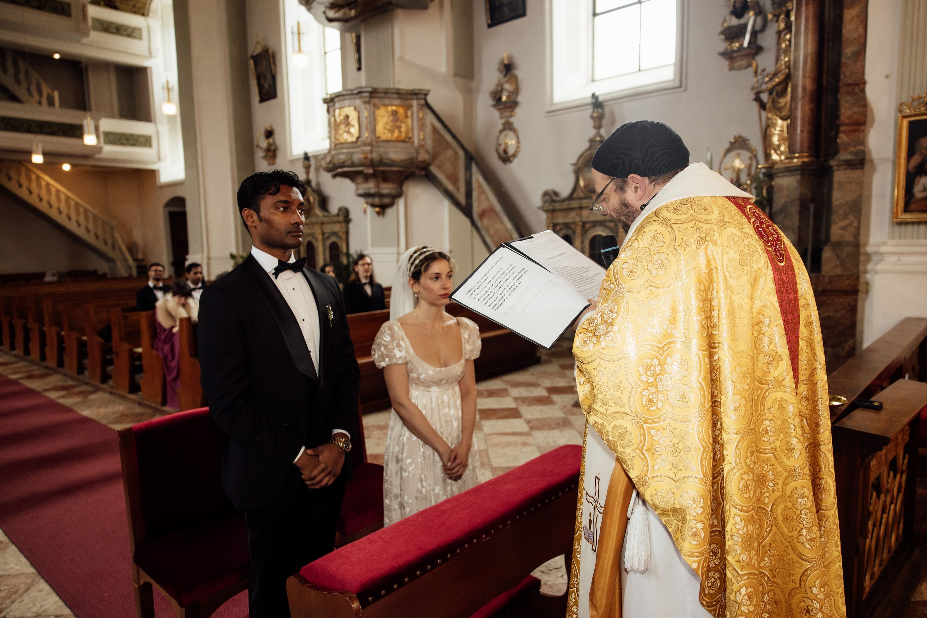 Bride and groom stand before the priest during a traditional church ceremony at a small wedding in Austria