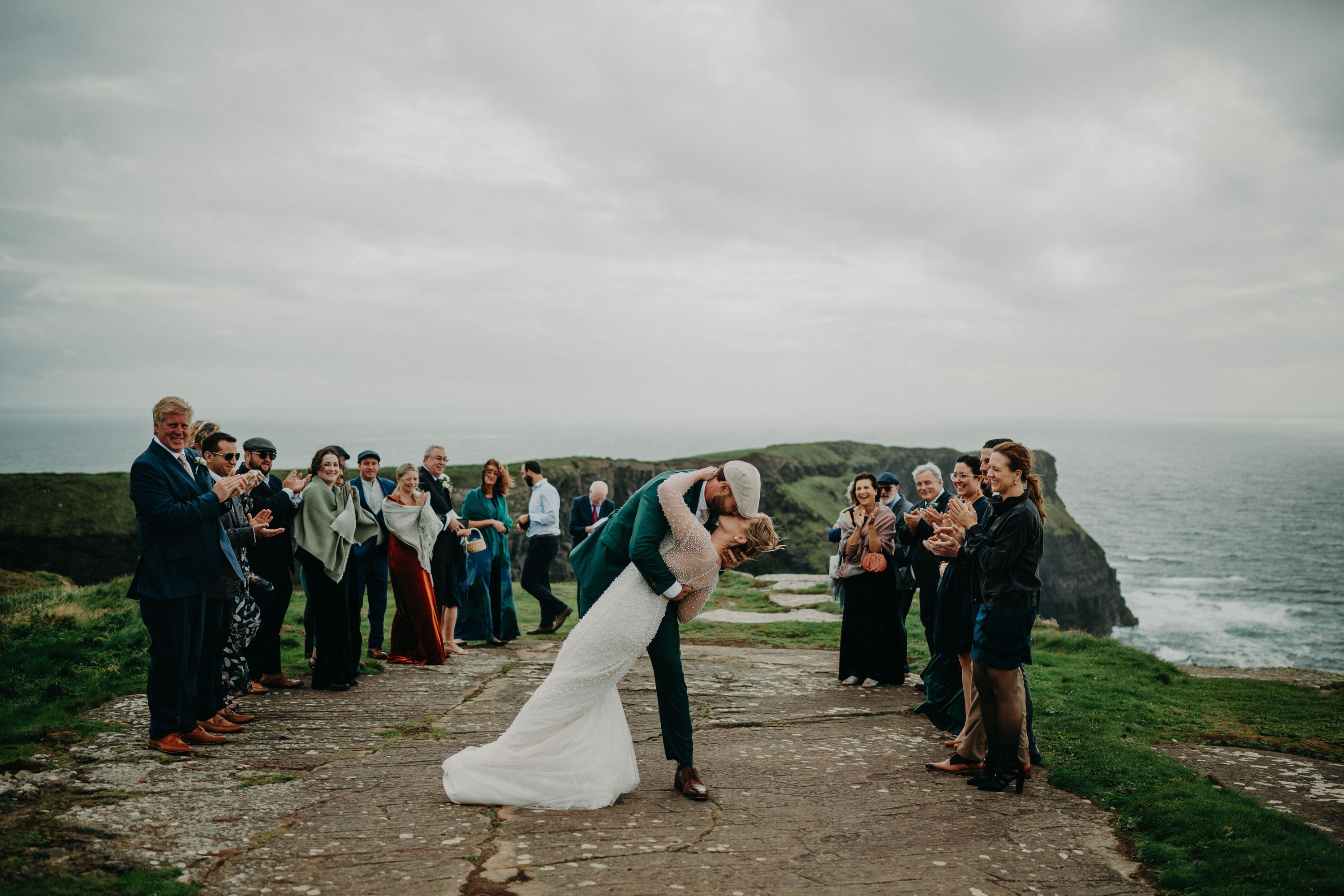 Newlyweds kiss in the middle of their guests who celebrate with them atop a cliff during their elopement in Ireland