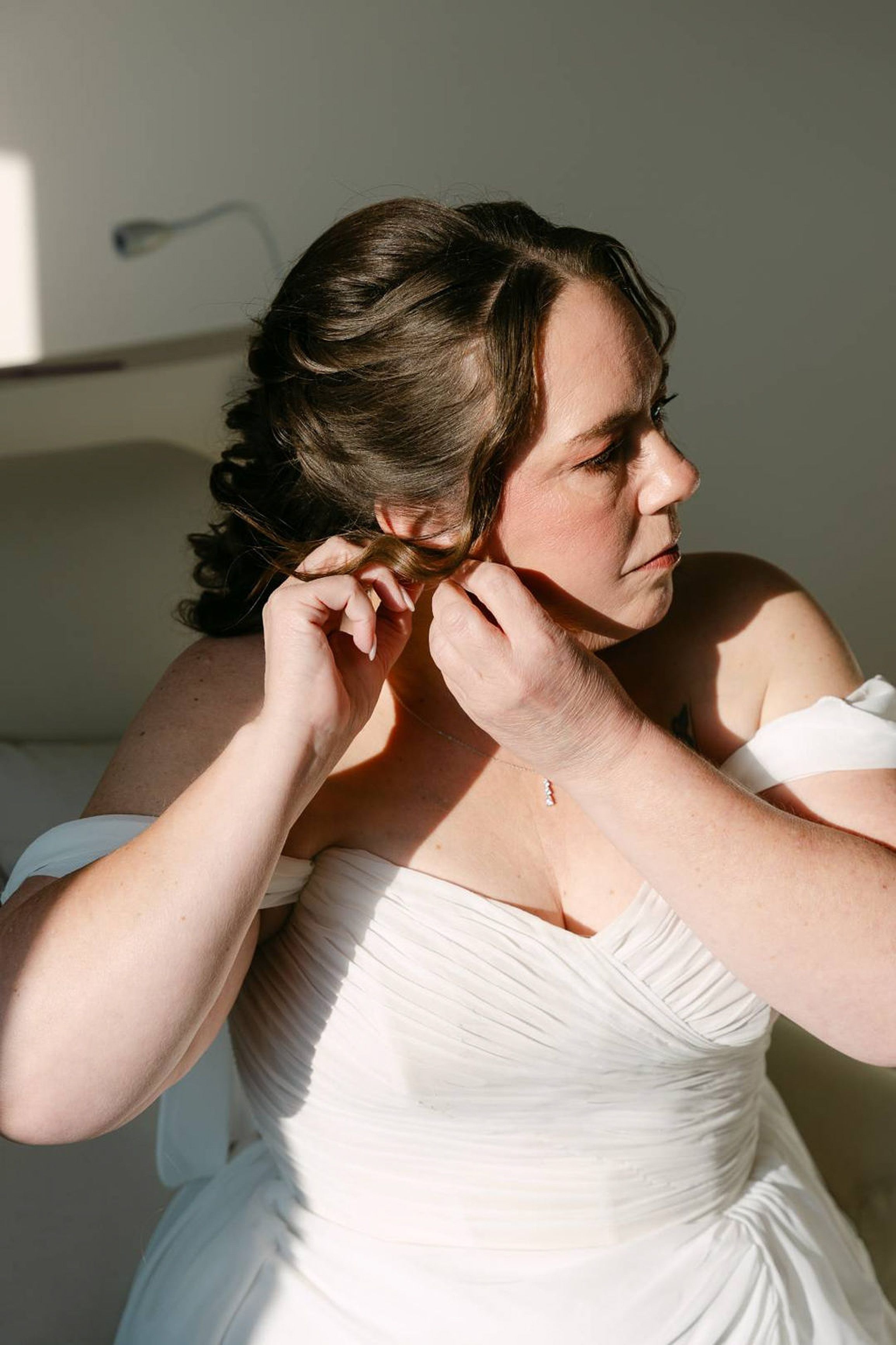 Bride fastening an earring in soft window light before an intimate wedding in Italy